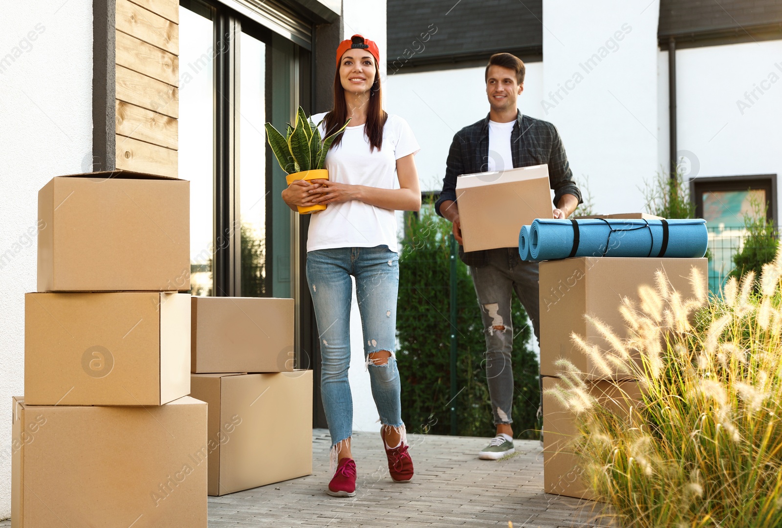 Photo of Happy couple with moving boxes and household stuff near their new house on sunny day