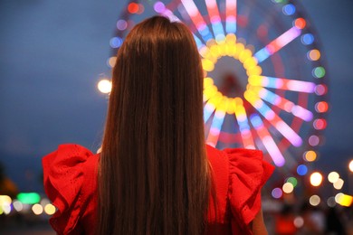 Photo of Beautiful young woman against glowing Ferris wheel in amusement park, back view