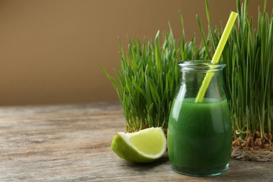 Photo of Glass bottle of wheat grass juice with citrus fruit and sprouts on wooden table. Space for text