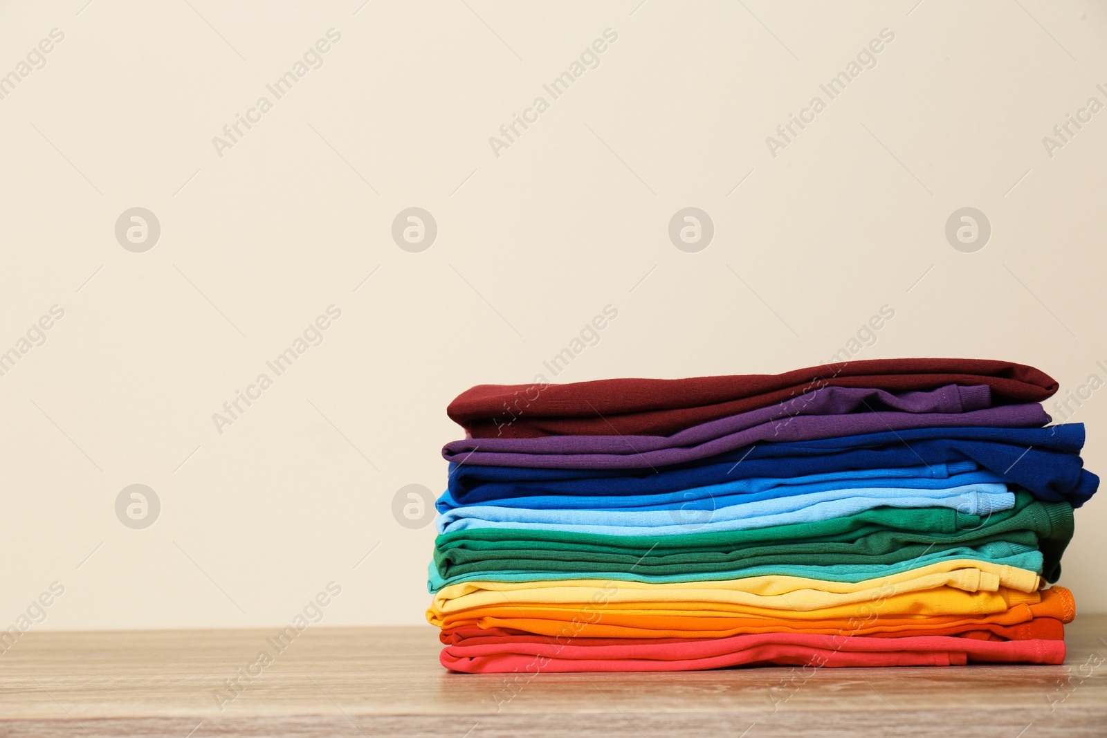 Photo of Stack of bright folded clothes on table against light background. Space for text