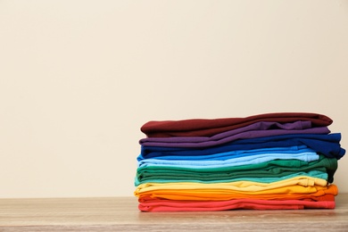 Stack of bright folded clothes on table against light background. Space for text