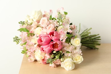 Photo of Beautiful bouquet of fresh flowers on wooden table near light wall