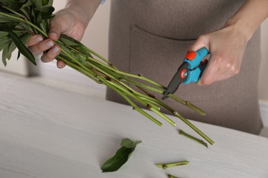 Photo of Florist cutting stems of flowers with pruner at workplace, closeup