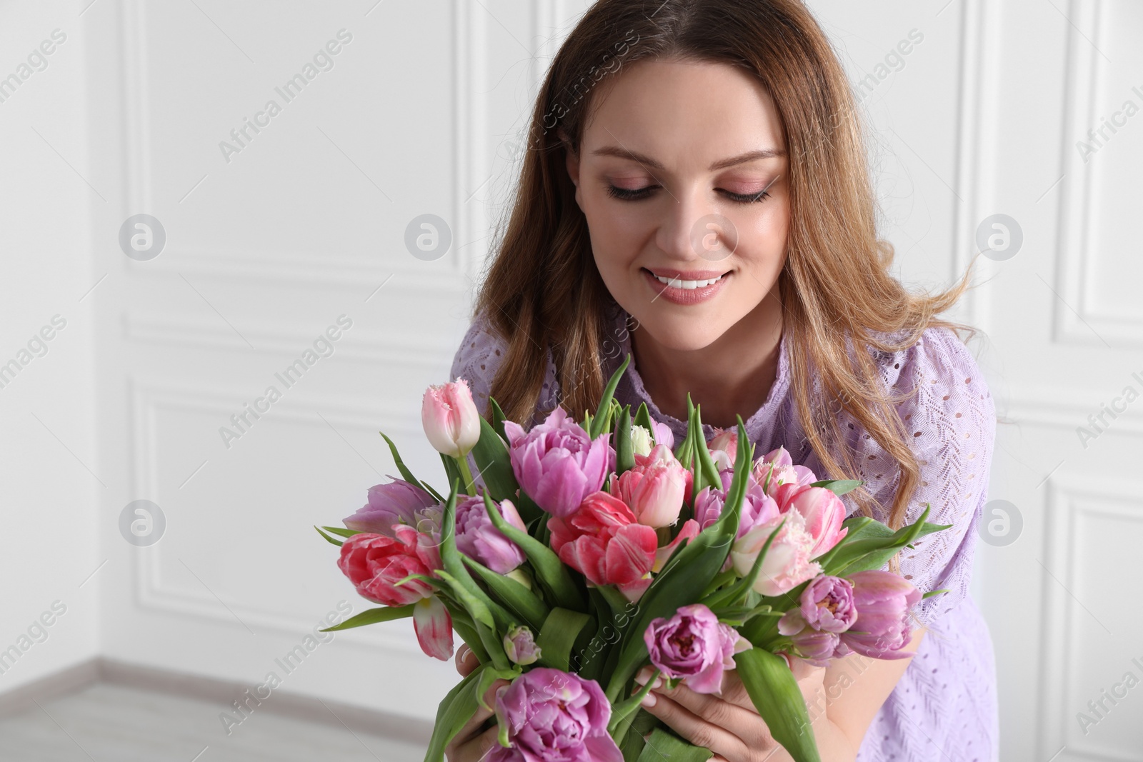 Photo of Young woman with bouquet of beautiful tulips indoors. Space for text