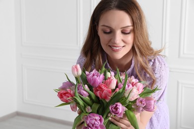 Young woman with bouquet of beautiful tulips indoors. Space for text