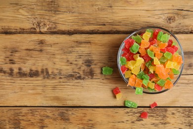 Mix of delicious candied fruits in bowl on wooden table, flat lay. Space for text