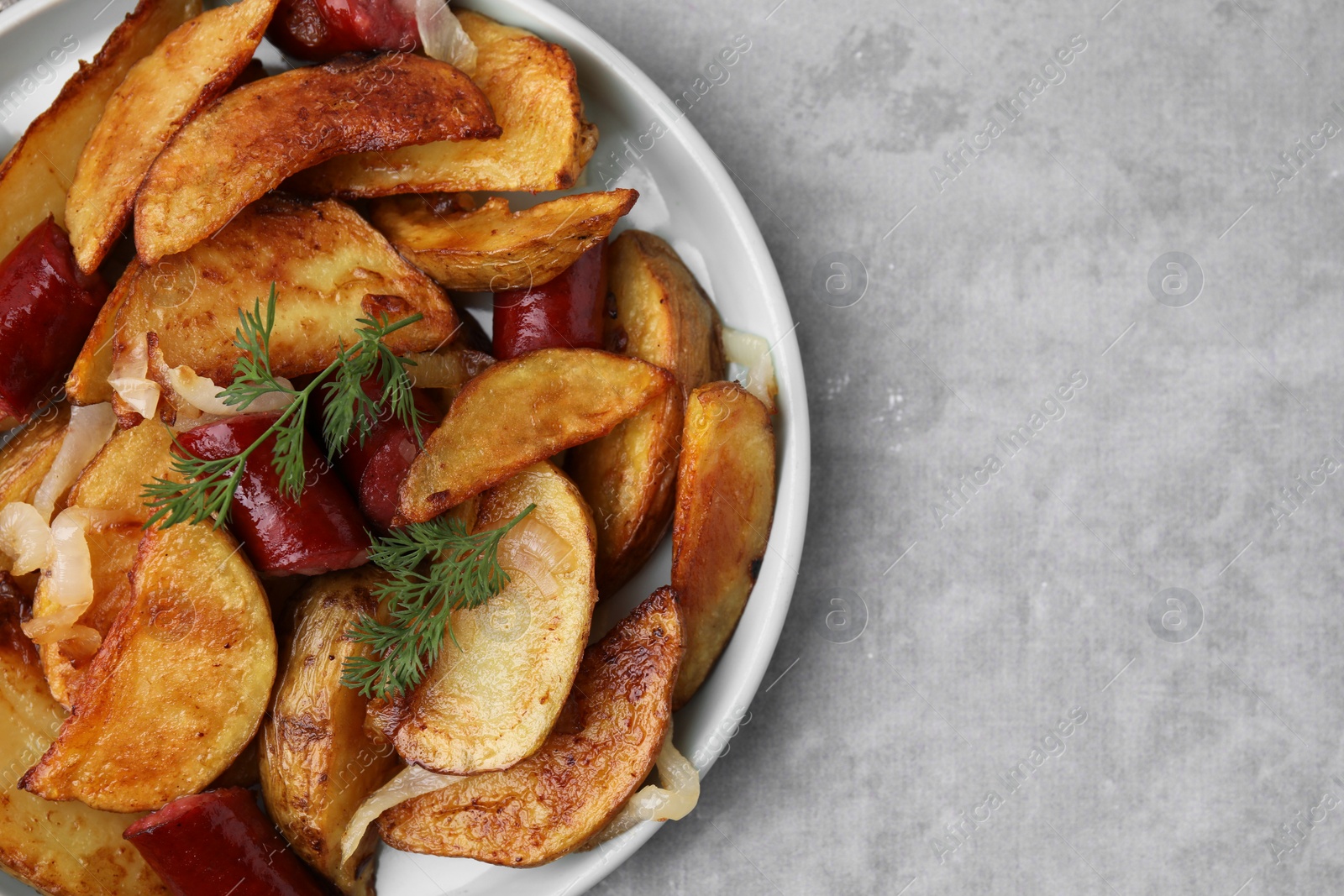 Photo of Delicious baked potato with thin dry smoked sausages, onion and dill on gray table, top view. Space for text