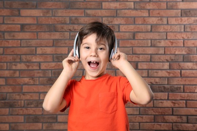 Photo of Cute little boy listening to music with headphones against brick wall