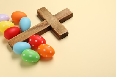 Photo of Wooden cross and painted Easter eggs on beige background, space for text