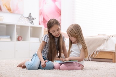 Cute little sisters reading book together at home