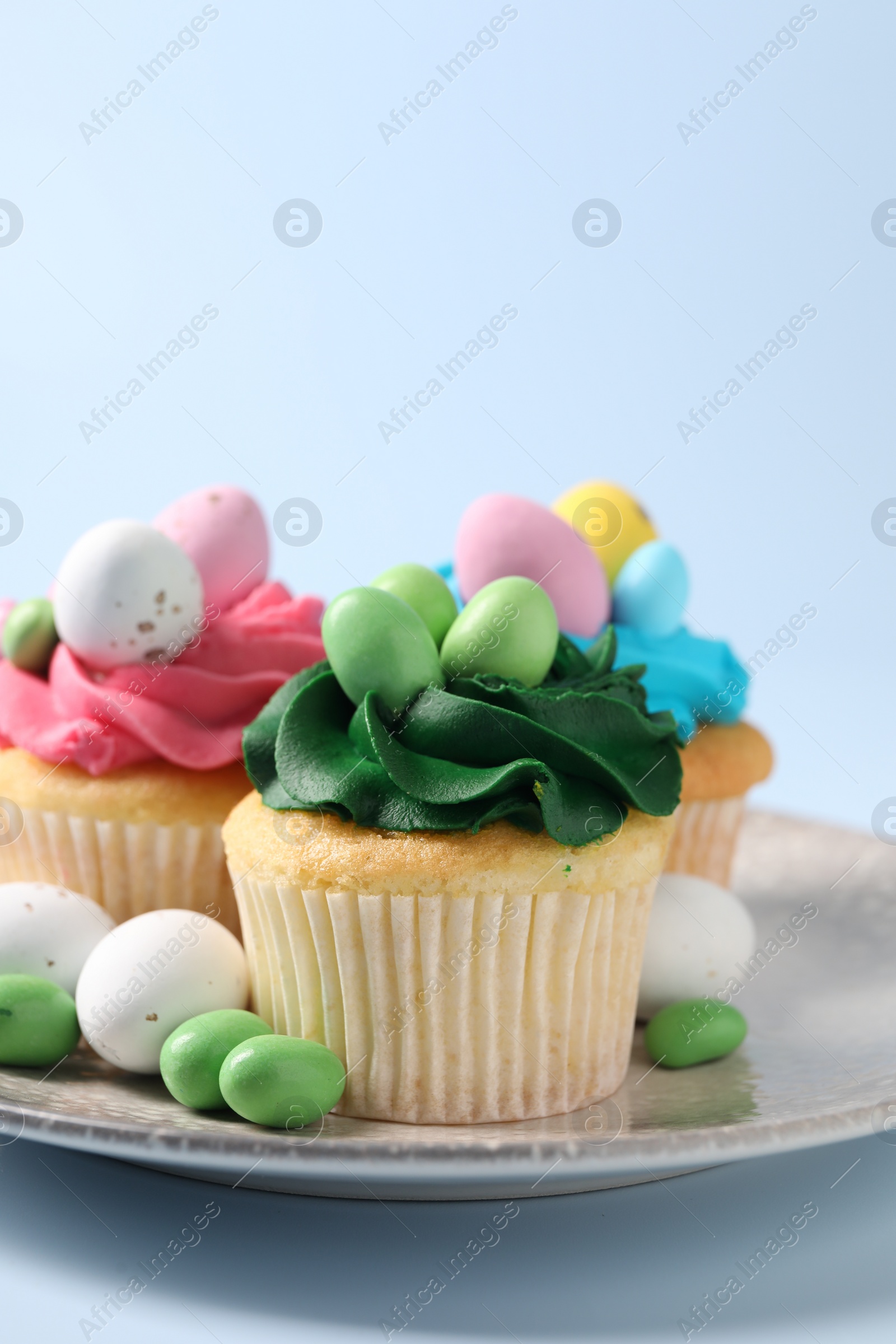 Photo of Tasty cupcakes with Easter decor on light blue background, closeup