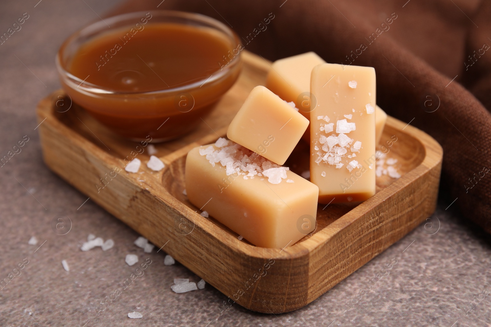 Photo of Yummy caramel candies, sauce and sea salt on brown table, closeup