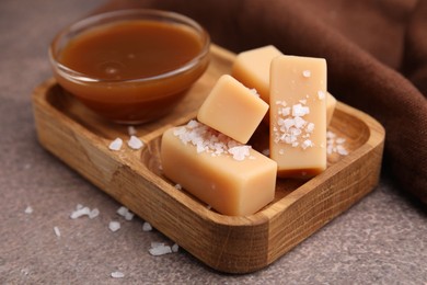 Yummy caramel candies, sauce and sea salt on brown table, closeup