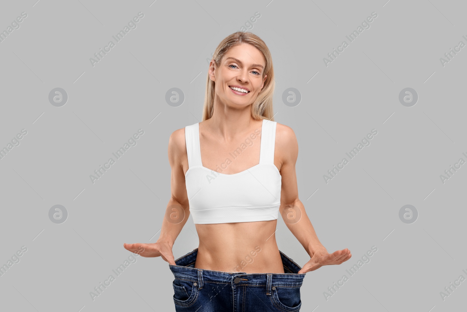 Photo of Slim woman wearing big jeans on grey background. Weight loss