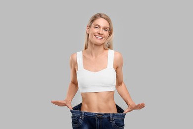 Photo of Slim woman wearing big jeans on grey background. Weight loss