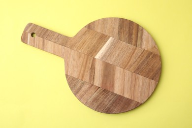 Photo of One wooden cutting board on yellow background, top view. Cooking utensil