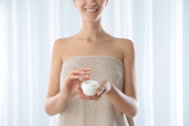 Photo of Young woman holding jar of cream at home, closeup