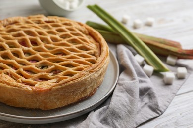 Freshly baked rhubarb pie, stalks and sugar cubes on light wooden table, closeup