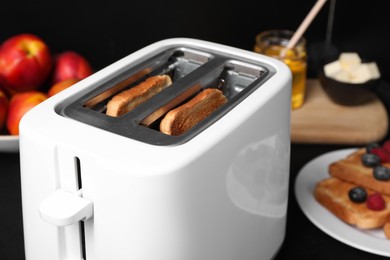 Photo of Modern toaster with slices of bread on table, closeup