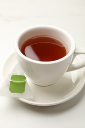 Tea bag and cup of hot beverage on white table, closeup