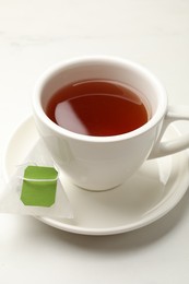 Photo of Tea bag and cup of hot beverage on white table, closeup