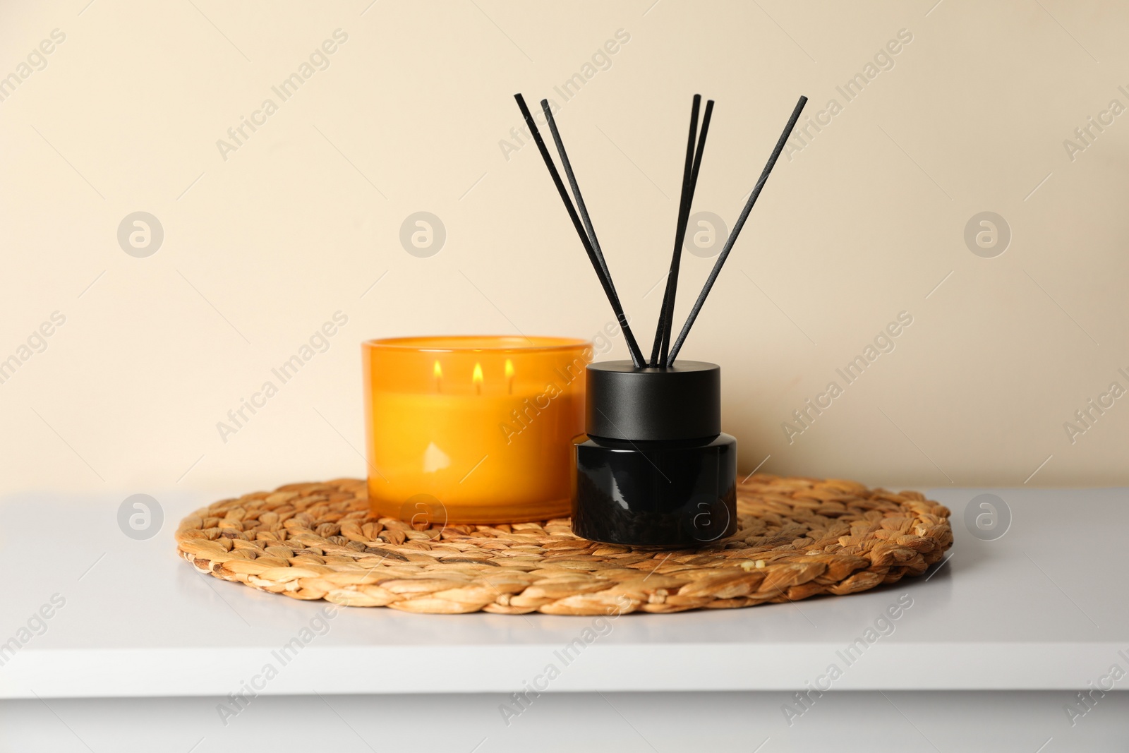 Photo of Aromatic reed air freshener and candle on white table indoors