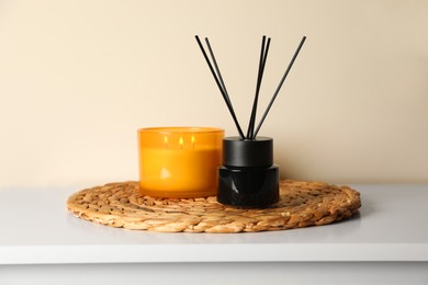 Photo of Aromatic reed air freshener and candle on white table indoors