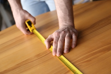 Photo of Man measuring wooden table, closeup. Construction tool