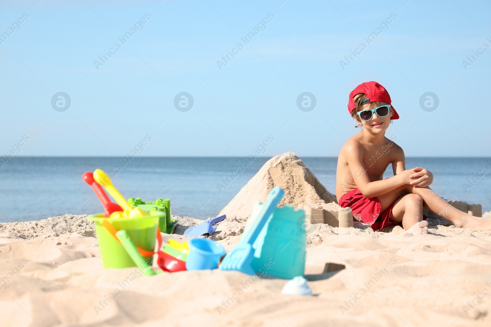 Photo of Cute little child and plastic toys at sandy beach on sunny day