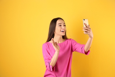 Woman using mobile phone for video chat on color background