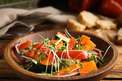 Salad with fresh organic microgreen in bowl on wooden table, closeup