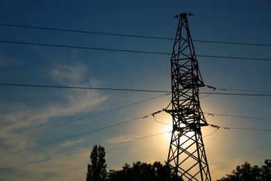 Photo of Silhouettes of high voltage tower and trees in evening