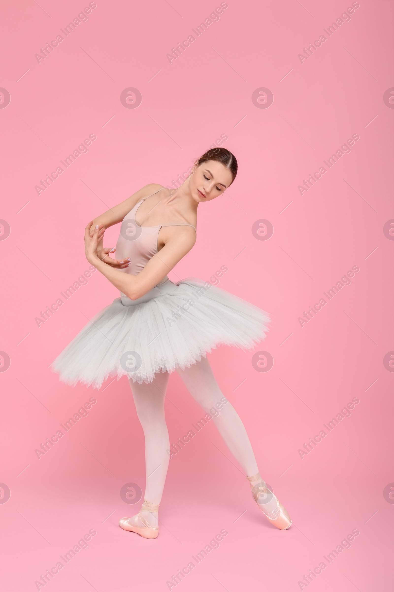 Photo of Young ballerina practicing dance moves on pink background