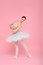 Young ballerina practicing dance moves on pink background