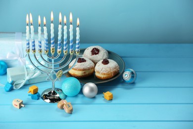 Photo of Composition with Hanukkah menorah, dreidels, donuts and gift boxes on table against light blue background. Space for text