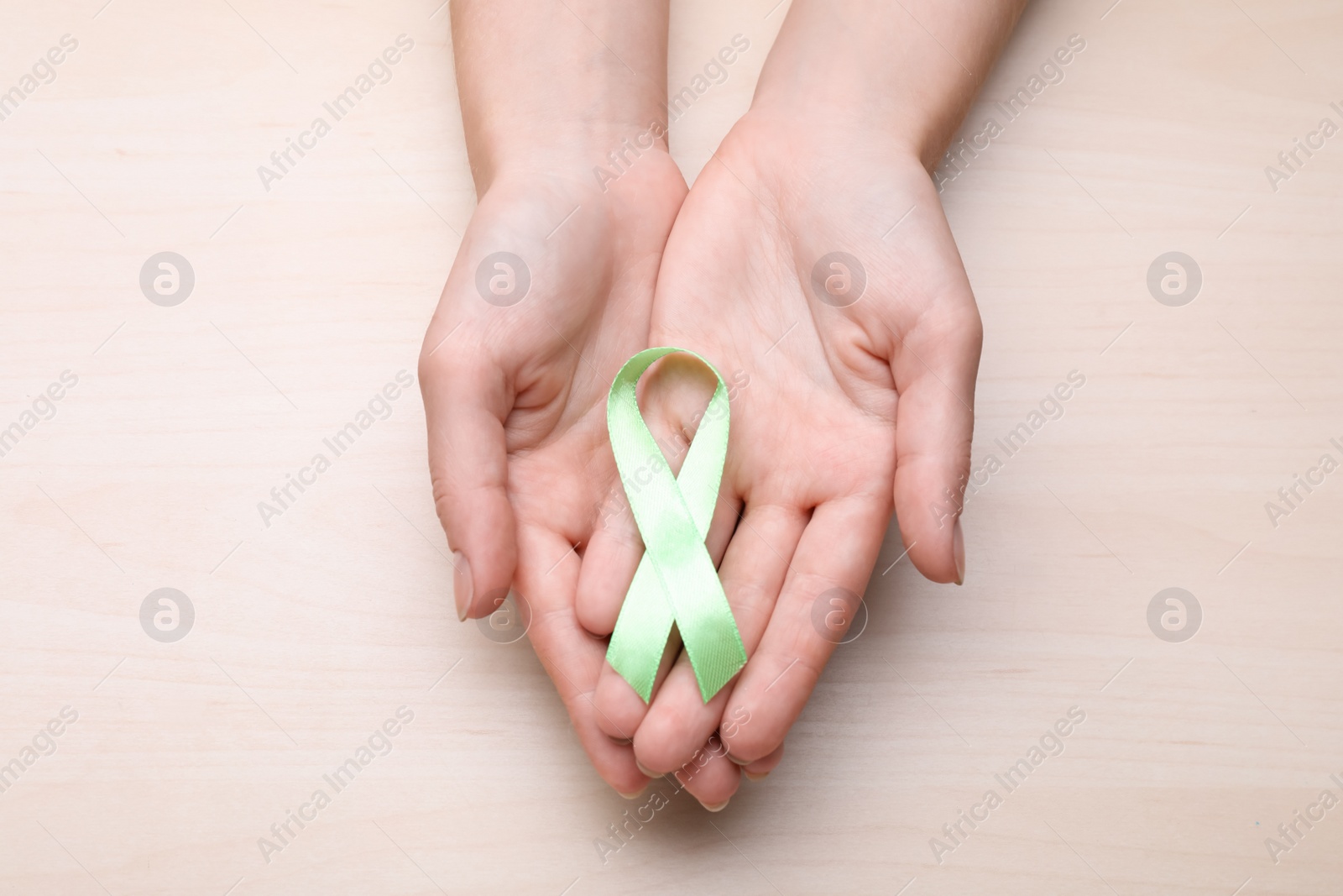 Photo of World Mental Health Day. Woman holding green ribbon on wooden background, top view