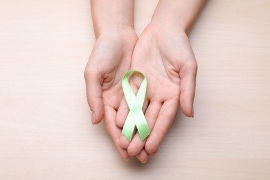 World Mental Health Day. Woman holding green ribbon on wooden background, top view