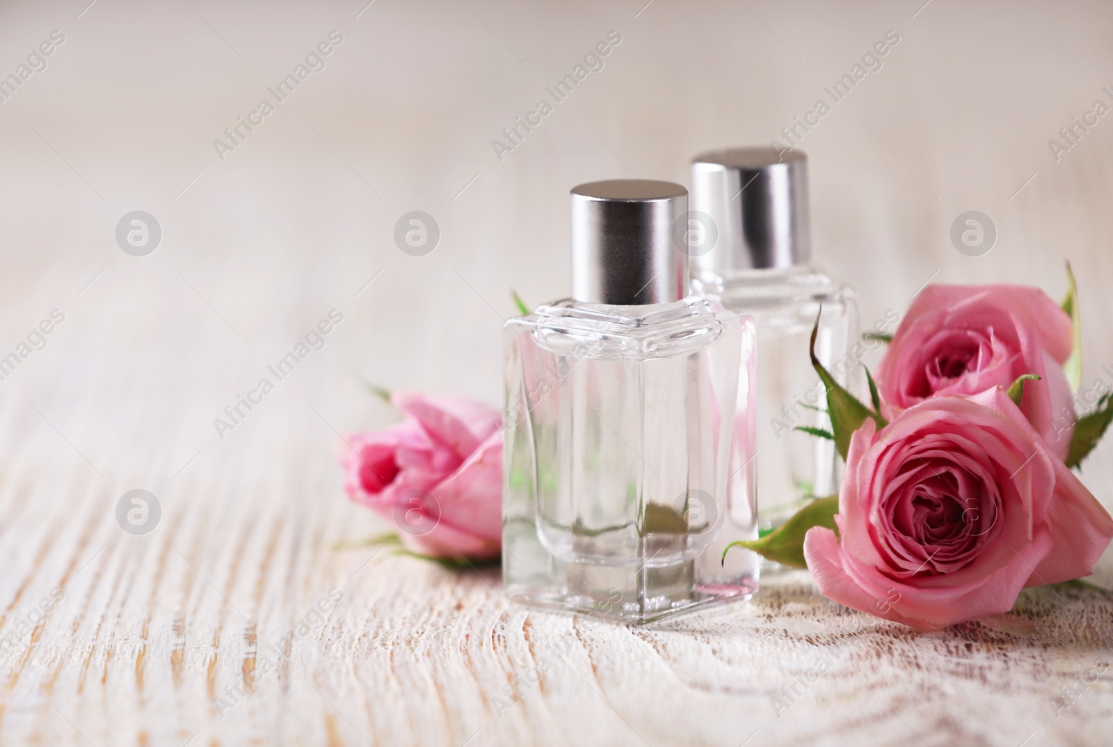 Photo of Bottles of essential oils and roses on white wooden table, space for text