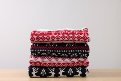 Photo of Stack of different Christmas sweaters on table against light background