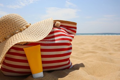 Photo of Tube of sunscreen, bag and hat on sand, space for text. Sun protection care