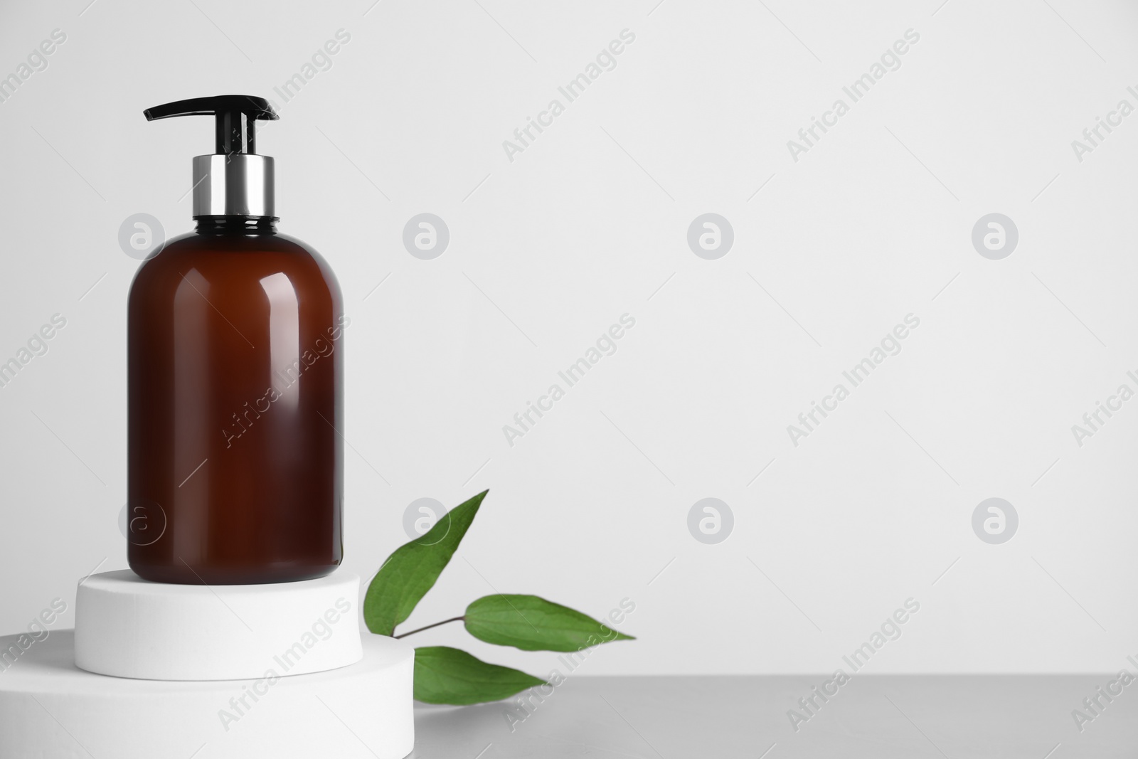 Photo of Bottle of cosmetic product and green leaves on light grey table against white background, space for text