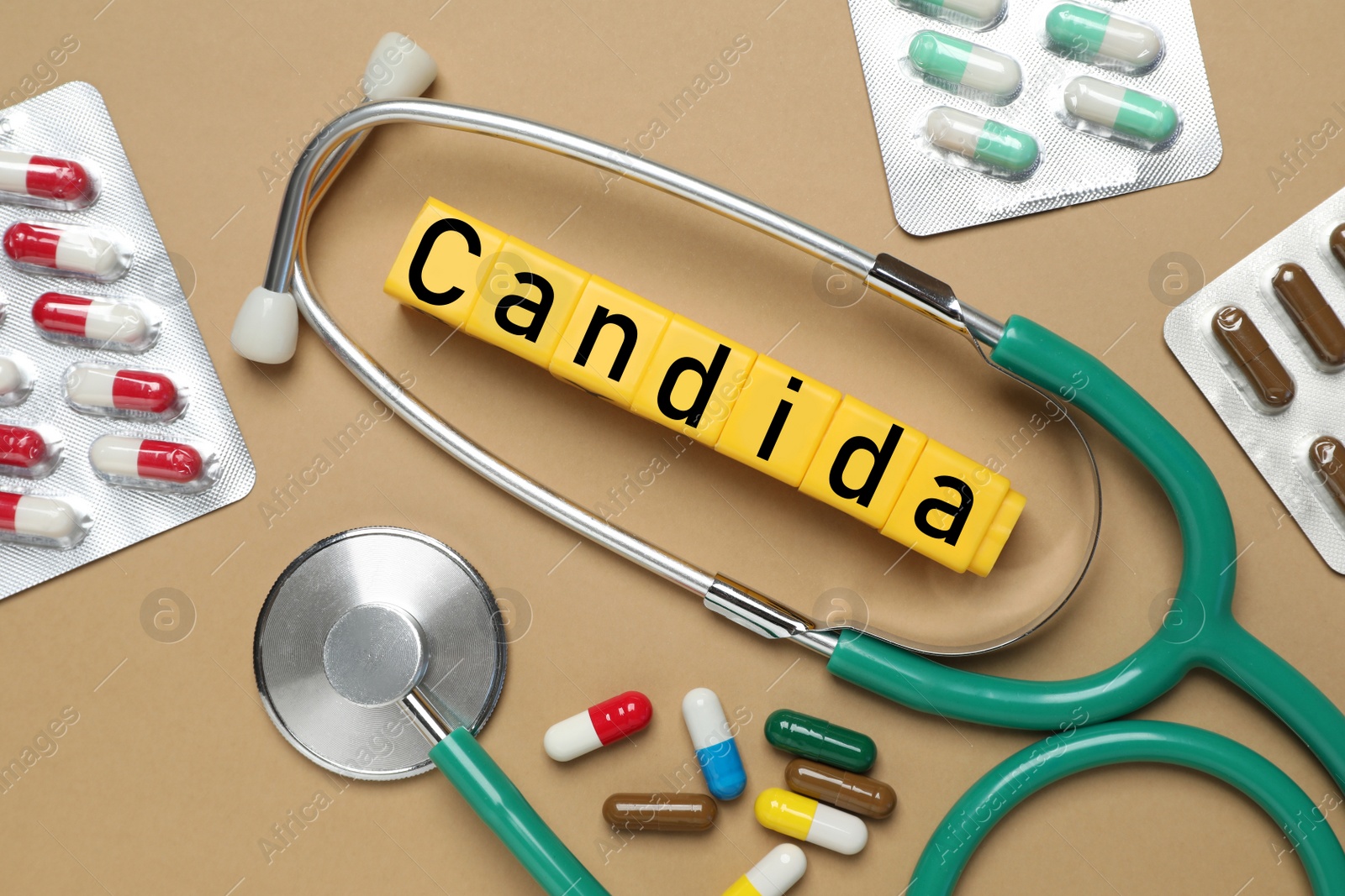 Image of Yellow cubes with word Candida, stethoscope and pills on light brown background, flat lay