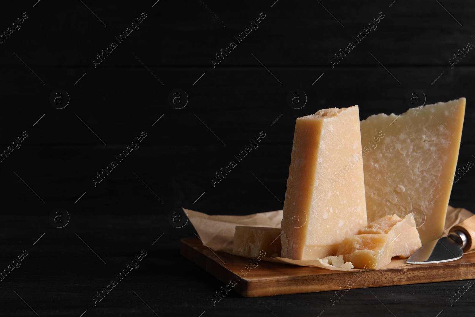 Photo of Parmesan cheese with board and knife on black wooden table. Space for text