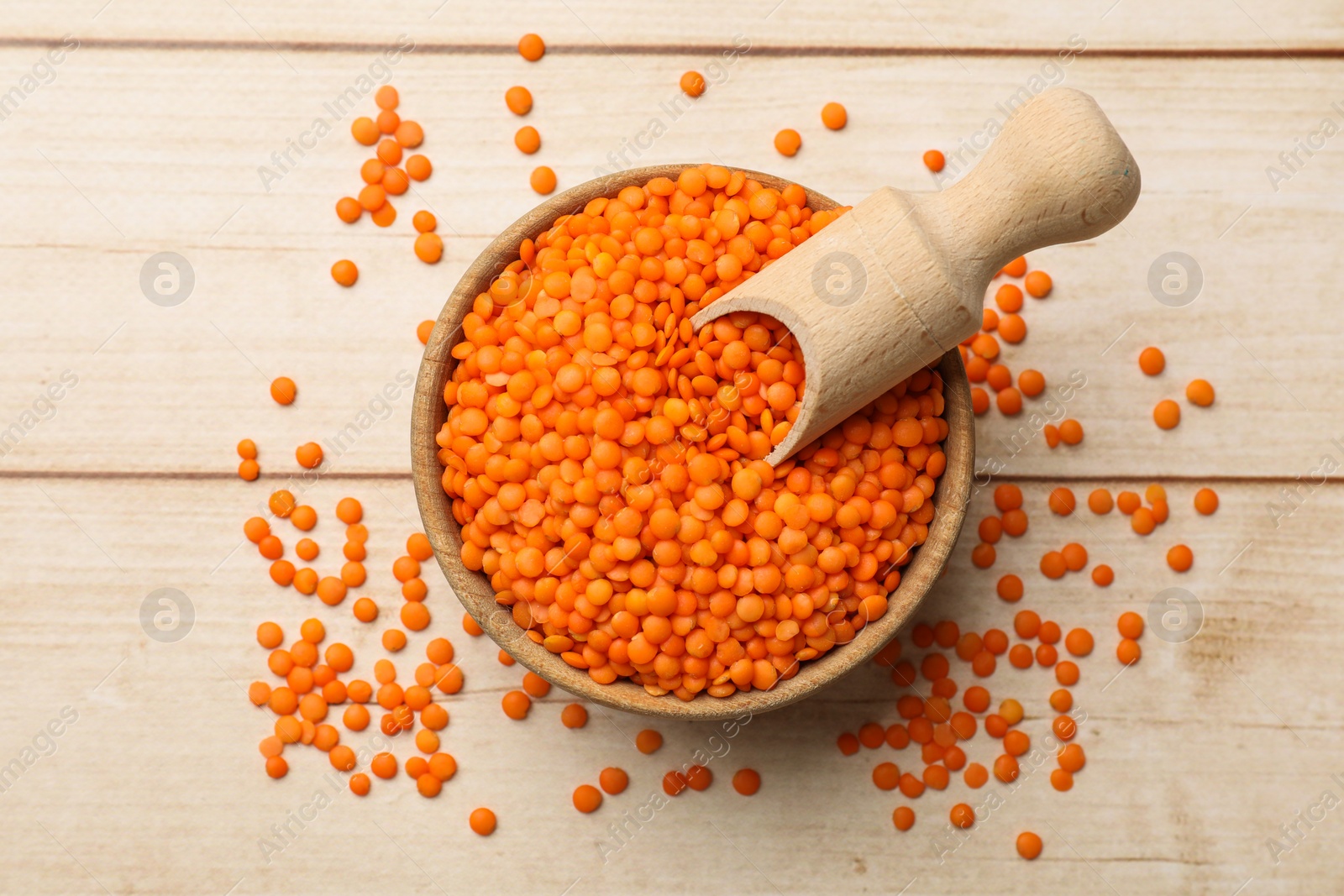 Photo of Raw red lentils in bowl on light wooden table, top view