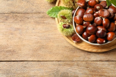 Fresh sweet edible chestnuts on wooden table, top view. Space for text