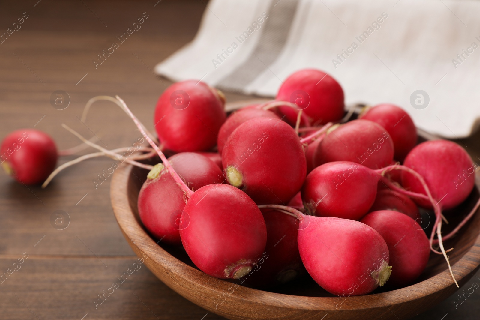 Photo of Bowl with fresh ripe radishes on wooden table, closeup