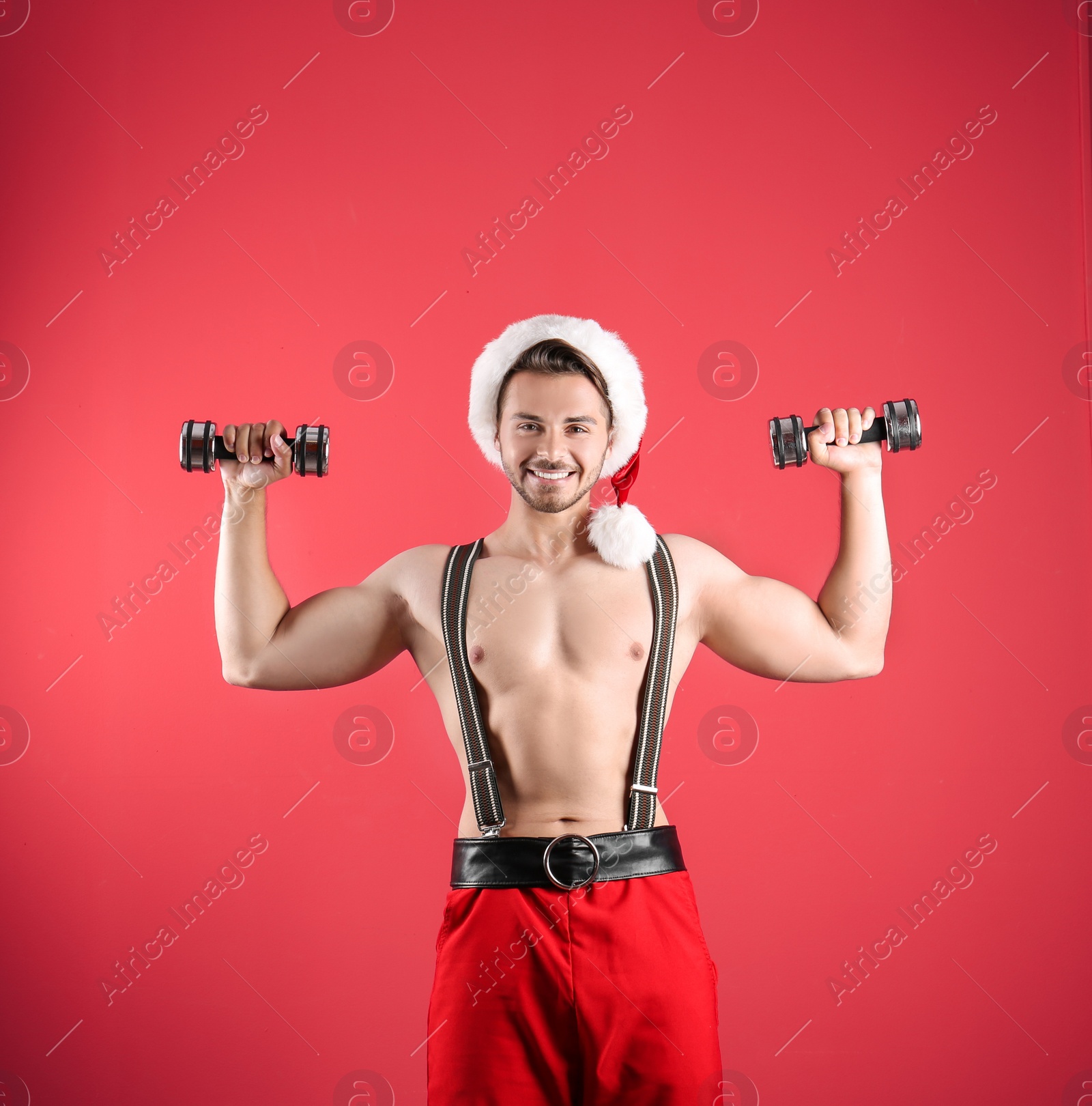 Photo of Shirtless sexy young Santa Claus with dumbbells on color background