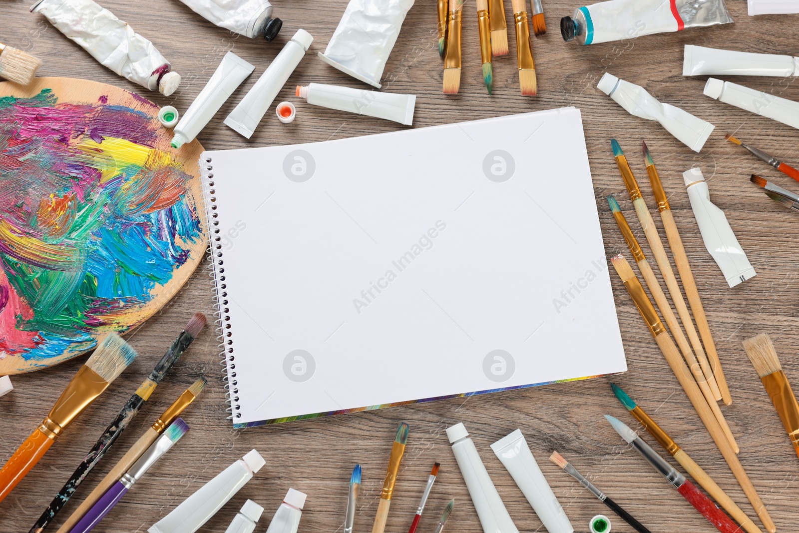 Photo of Blank sketchbook, set of brushes and paints on wooden table, flat lay. Space for text