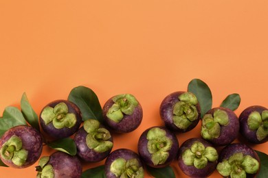 Photo of Fresh ripe mangosteen fruits with green leaves on orange background, flat lay. Space for text