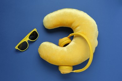 Photo of Yellow travel pillow, headphones and sunglasses on blue background, flat lay